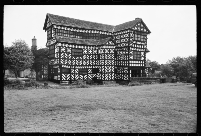 Little Moreton Hall, near Congleton, Cheshire, c1955 c1980. Creator: Ursula Clark. Little Moreton Hall, near Congleton, Cheshire, c1955 c1980. Exterior view of Little Moreton Hall taken from the south west. At the far right side is the three storeyed gabled porch that reaches the single span ashlar bridge that crosses the moat. To the left of the porch is a garderobe tower of two storeys, and to the left again a double jettied long section of two storeys. The roof reaches the bottom of the window sill of the gallery behind, which has 32 windows separated into sections of seven. The western end of this southern front is visble, and consists of three storeys, of which all are jettied, and a gable. The house was built between the early 15th to 16th centuries in seven stages, and presented as a range of buildings around an interior courtyard and is surrounded by a moat. The property is now owned by the National Trust.
