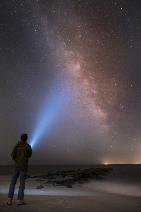 Asian man shining flashlight on starry sky,Cape May, New Jersey, USA Asian man shining flashlight on starry sky