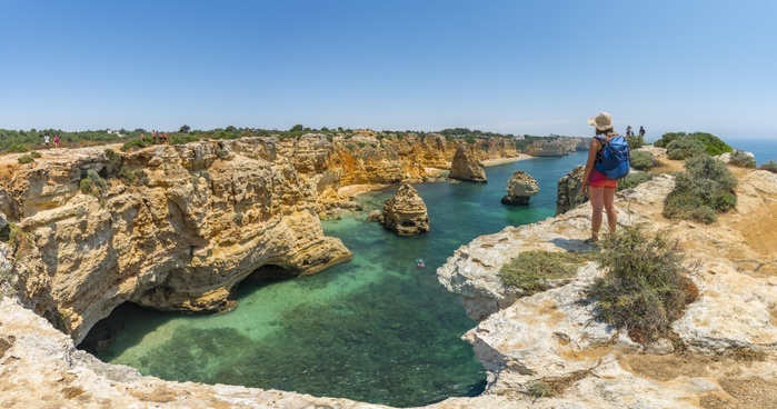Portugal Sea Young woman standing on rocks at steep coast, view over turquoise sea, beach Praia da Marinha, jagged rocky coast of sandstone, rock formations in the sea, Algarve, Lagos, Portugal, Europe, Photo by Moritz Wolf