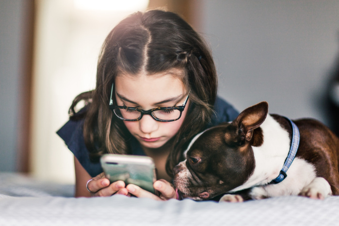 Girl using smartphone beside pet dog on bed