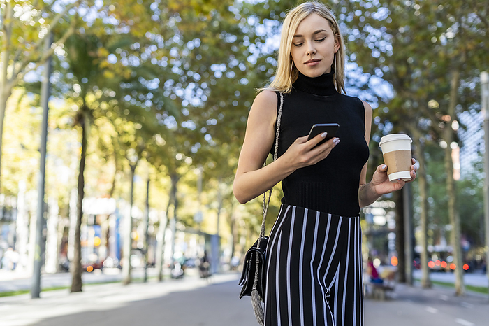 young woman Portrait of blond woman with coffee to go looking at cell phone