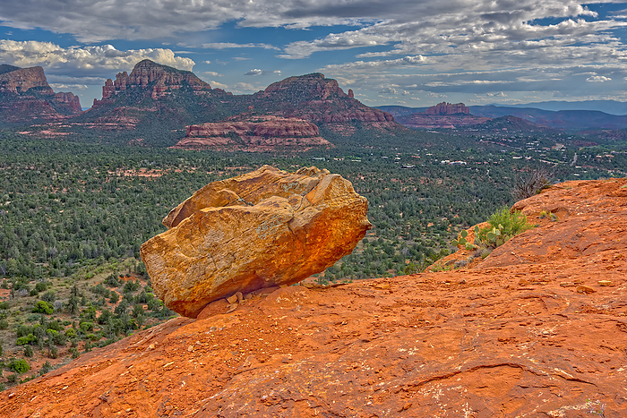 A boulder balanced on the edge of a cliff in Sedona. In the distance are the Twin Buttes and Cathedral Rock. A boulder balanced on the edge of a cliff in Sedona with the Twin Buttes and Cathedral Rock in the distance, Arizona, United States of America, North America, Photo by Steven Love