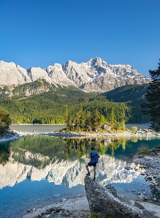Germany Hiker standing on rocks, view into the distance, Zugspitze and Wetterstein range with reflection in the Eibsee lake, near Grainau, Upper Bavaria, Bavaria, Germany, Europe