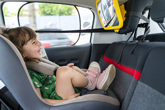 Laughing toddler girl sitting in a car seat looking in a mirror Laughing toddler girl sitting in a car seat looking in a mirror