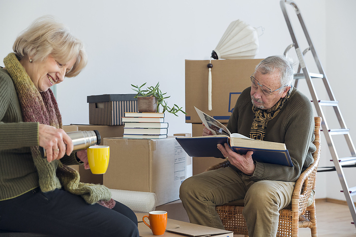 senior couple Senior couple with photo album and hot drink surrounded by cardboard boxes in an empty room