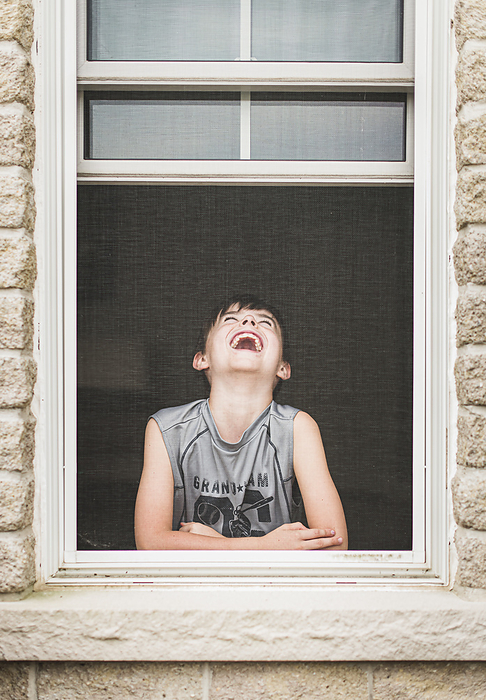 Young boy laughing in an open window shot through the screen.