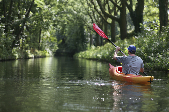 canoe A caucasian man kayaking along a river shaded by a tree canopy