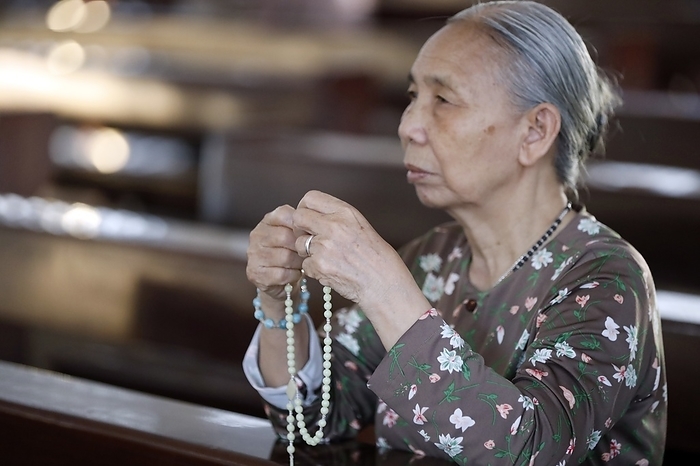 Asian woman praying the rosary in a catholic church.  Ba Ria. Vietnam. 