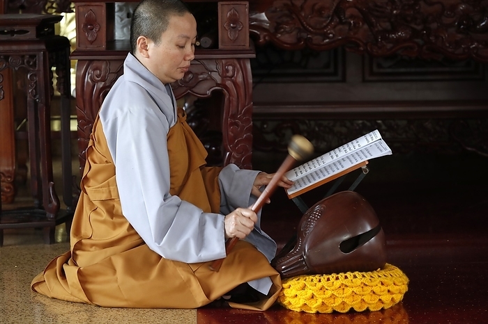 Buddhist ceremony at temple. Monk playing on a wooden fish (percussion instrument). Ho Chi Minh city. Vietnam. 