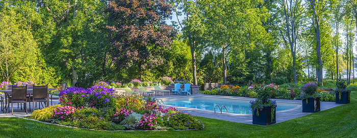 Residential swimming pool in a backyard with blossoming flowers and full trees; Hudson, Quebec, Canada, Photo by David Chapman