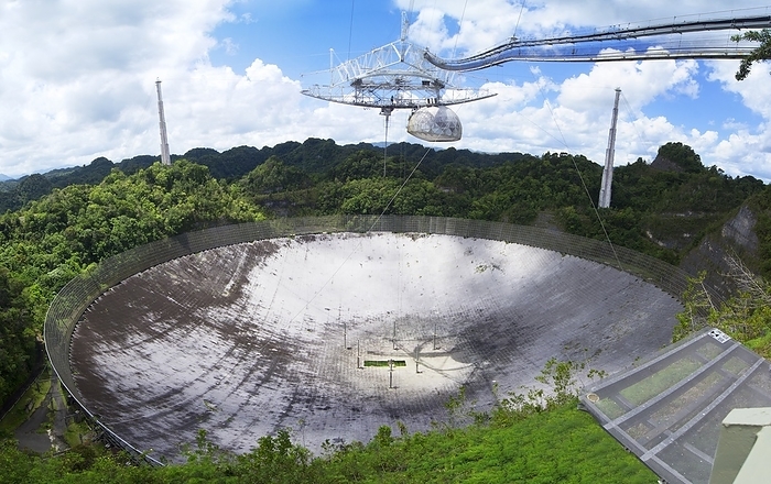 Arecibo Observatory, Puerto Rico A panoramic view of the main antenna dish of the Arecibo Observatory in Puerto Rico. The large antenna reflector  305m in diameter  was the world s largest radio telescope for many years and is suspended in a natural hollow in the limestone scenery. The radio telescope s main feed can be seen above the antenna. The radome houses the Gregorian sub reflector, which corrects for the non parabolic shape of the main reflector. Surrounding the antenna is a ground screen designed to screen out terrestrial radio interference that would otherwise disrupt the operation of the telescope. Arecibo is also known for its use in the search for extraterrestrial intelligence  SETI . An example of the 38000 aluminium panels that form the reflecting surface is displayed at right.
