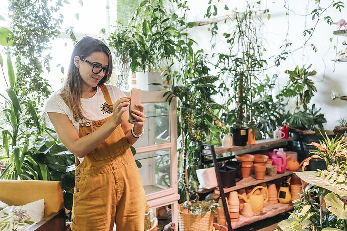 Young woman taking smartphone picture in a small gardening shop Young woman taking smartphone picture in a small gardening shop