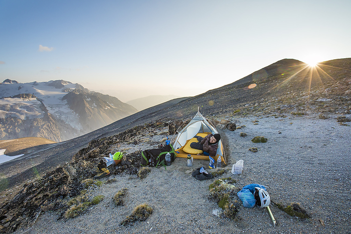 Athelney Pass, British Columbia, Canada Man pokes head out of tent at sunset while camping on mountain ridge.