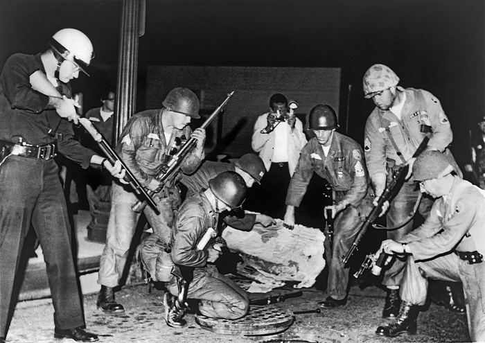 Los Angeles, California,  August 18, 1965.   
A heavily-armed group of police and National Guardsmen stand ready at an open manhole after dropping a tear gas shell inside. Shooting suspects were believed to be using the storm sewer system to escape capture after a gun battle between the police and Black Muslims.