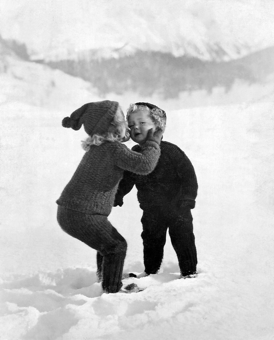 United States:  c. 1922.
A very young girl gives her little brother a kiss on the cheek in the snow.