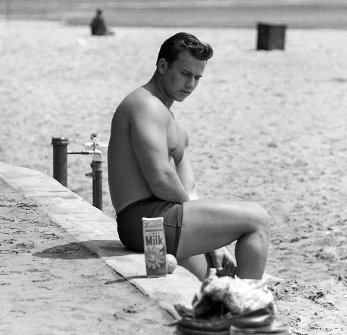 San Francisco, California: c. 1953.
A well muscled man on the beach contemplates his quart of Bordens milk.