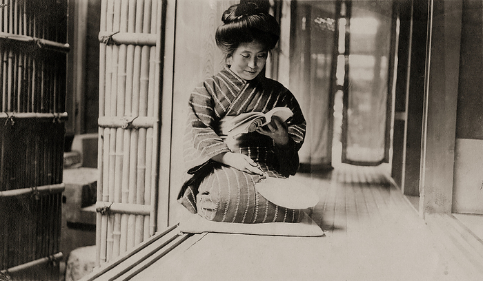 160305 0043   Woman Reading a Book A Japanese woman in a striped kimono is reading a book on the engawa    , a veranda like extension of the house  of a private home. She is holding an uchiwa fan.  Photo by MeijiShowa AFLO