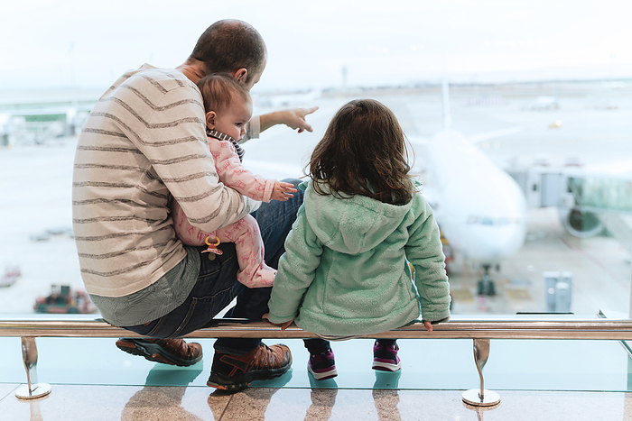 Father with two daughters sitting at the airport in front of a plane