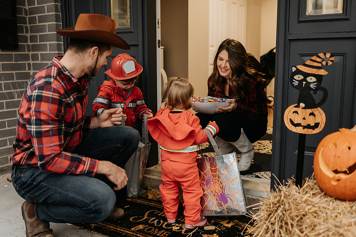 A family dressed up for Halloween trick or treating, collecting sweets from a woman at her door. A family dressed up for Halloween trick or treating, collecting sweets from a woman at her door.