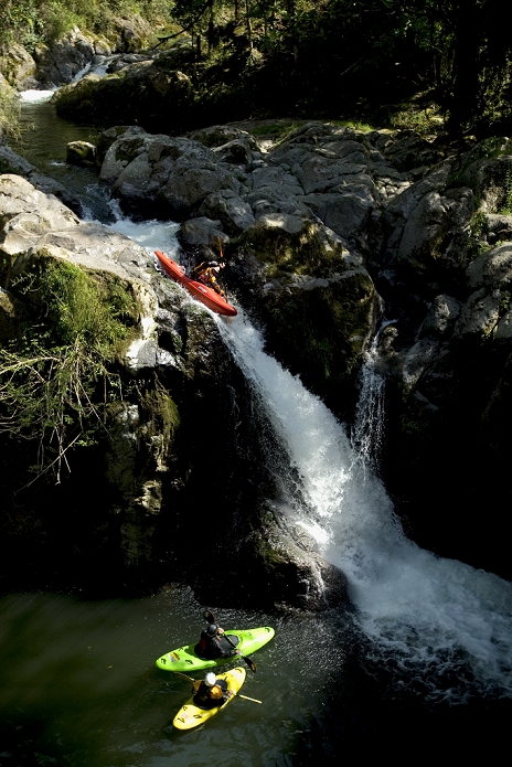 Two kayakers watching another kayaker go off of a waterfall.