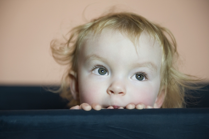 Baby girl peering over side of crib, portrait