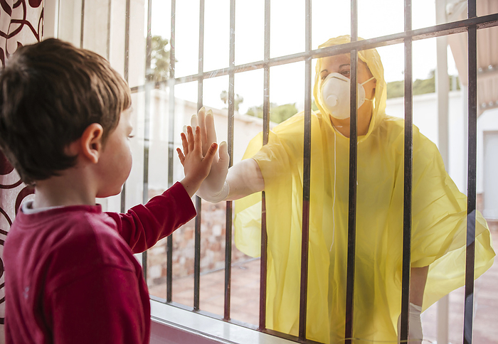 parent and child Boy touching mother s hand wearing protective clothing behind windowpane