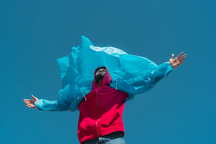 Young man wearing plastic rain coat, stanind in gthe wind with arms outstretched