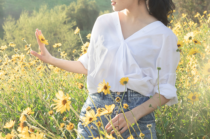 Brunette woman holding yellow daisy in flower field in the sunlight, Los Angeles, CA, United States