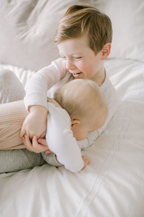 Toddler boy and baby sister playing on bed at home, San Jose, CA, United States