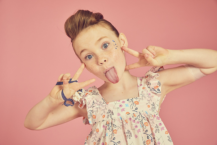 Portrait of brunette girl wearing frilly dress with floral pattern on pink background, sticking out tongue at camera. Portrait of brunette girl wearing frilly dress with floral pattern on pink background, sticking out tongue at camera.