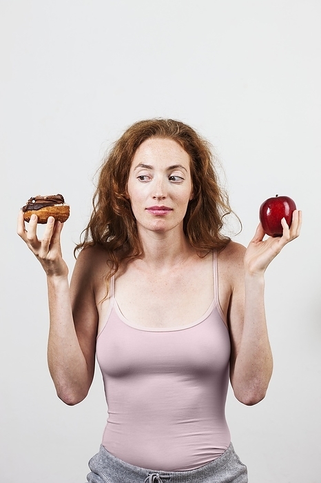 Portrait of woman holding apple and doughnut Indecisive woman holding apple and doughnut.