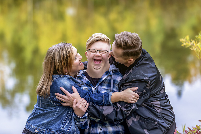 family A young man with Down Syndrome being teased and hugged by his father and mother while enjoying each other s company in a city park on a warm fall evening: Edmonton, Alberta, Canada