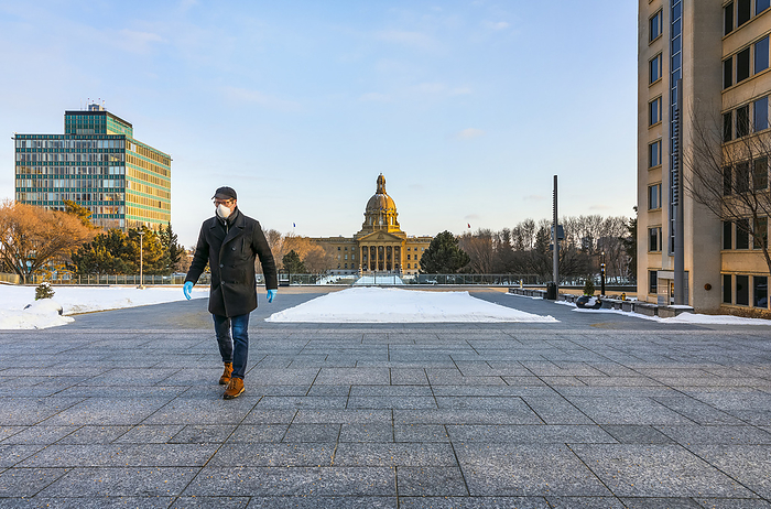 A man wearing a mask and gloves walks on a path by the Legislature during the Covid-19 world pandemic; Edmonton, Alberta, Canada