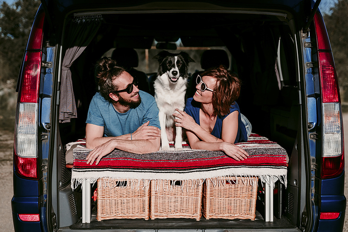 Relaxed couple with dog lying in the boot of a minivan