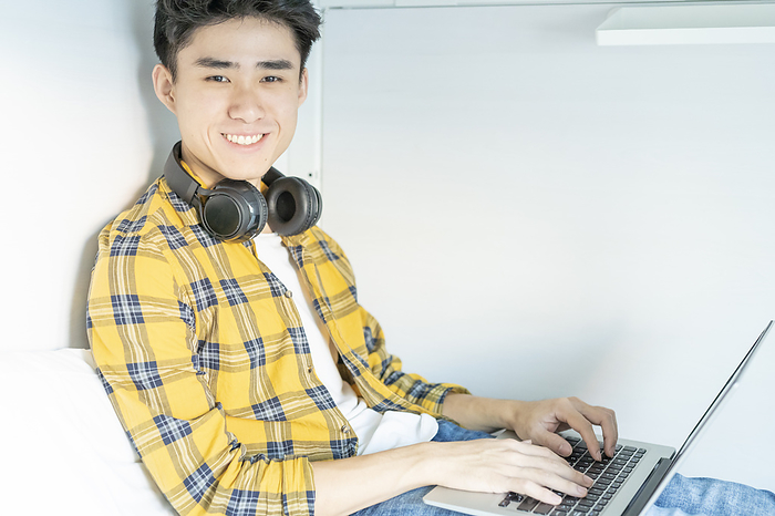Portrait of smiling young man with headphones sitting on bed using laptop