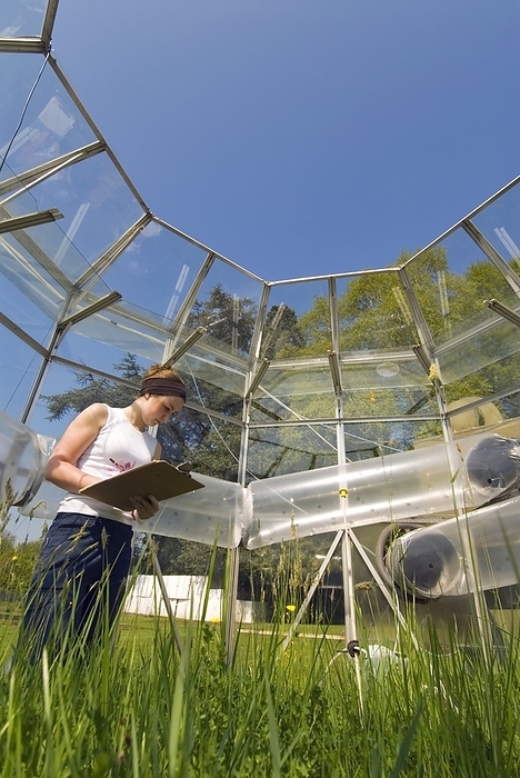 Chamber for pollution research Chamber for pollution research. Researcher noting the heights of plants in a simulated haymeadow grassland of conservation value. The plants are kept in a fumigation chamber that produces controlled exposure to the pollutant gas, ozone. The gas is pumped in through the wide polythene tubes running around the outside. The chamber replicates the present and projected ozone climates, and changes in species composition are monitored. Photographed at Close House field station, Newcastle University, UK.