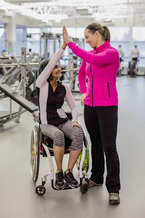 A paraplegic woman and her trainer give a high five after a successful workout in a recreational facility: Sherwood Park, Alberta, Canada
