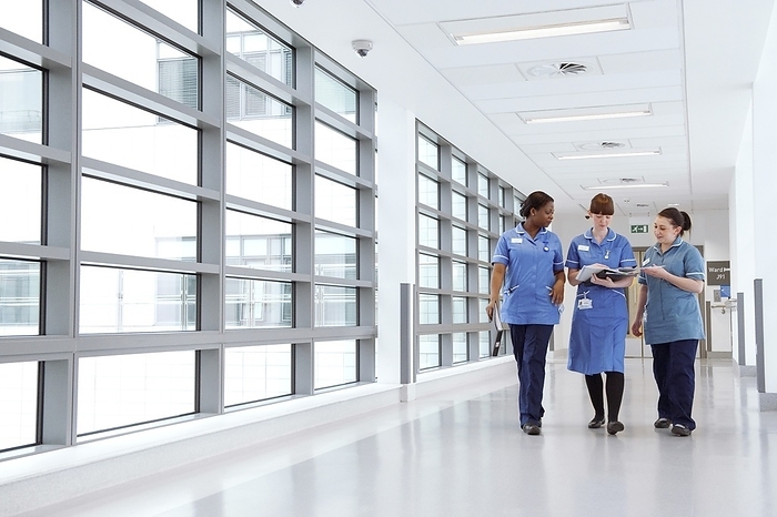 Nurses walking along hospital corridor Nurses walking along a hospital corridor discussing a patient s notes.