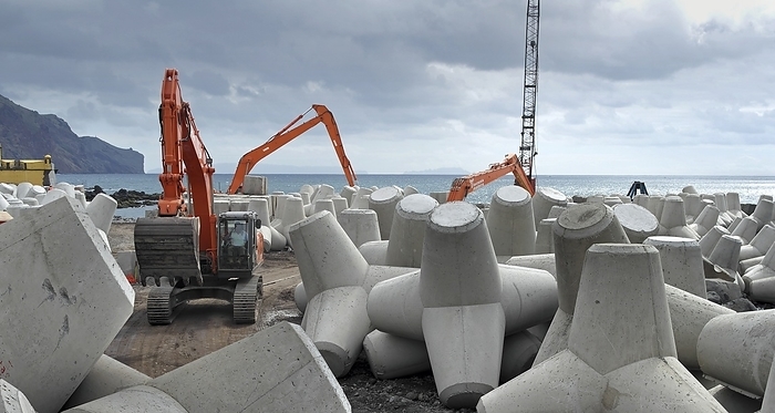 Coastal defence construction, Portugal Coastal defence construction. Precast concrete blocks being lined up along a shore. This type of sea defence is known as rock armour. The piles of concrete dissipate the energy of the waves, reducing coastal erosion. Photographed in Madeira, Portugal.
