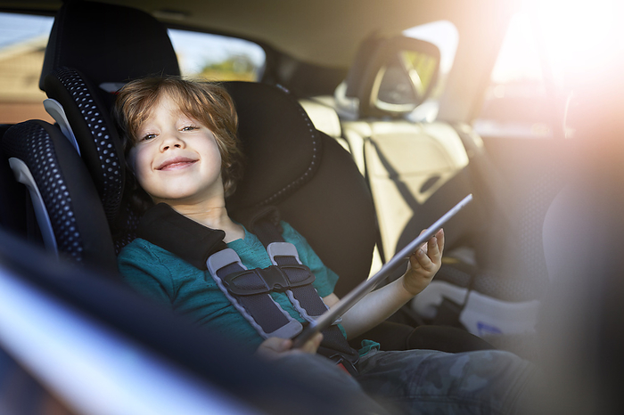Portrait of smiling boy using digital tablet while sitting at back seat in car Portrait of smiling boy using digital tablet while sitting at back seat in car