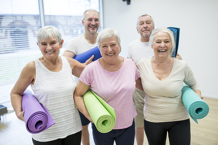 Group of happy seniors holding mats for yoga class