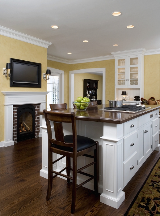 KITCHEN: Island with tall bar chairs, cooktop, yellow painted wall , white trimwork, flat screen tv over fireplace,