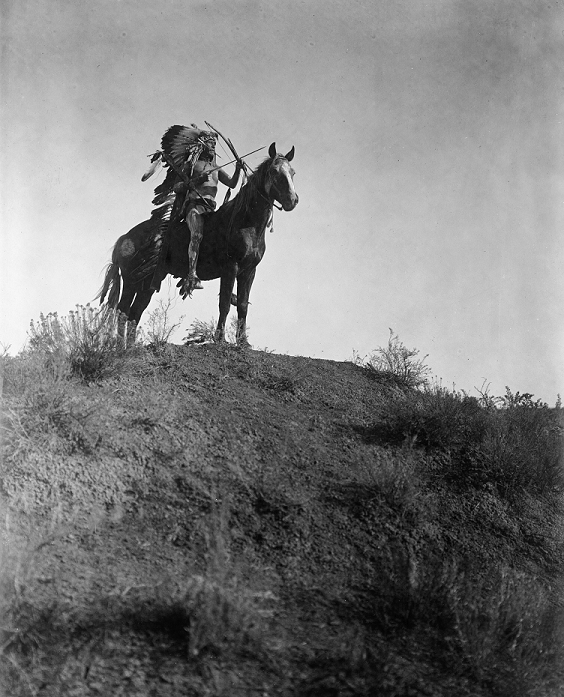 People of the World America Indigenous Indians  1908  Native American Indian man in feather headdress, on horseback, holding bow and arrows, 1 arrow in his mouth, 1908. Photograph by Edward Curtis  1868 1952 .