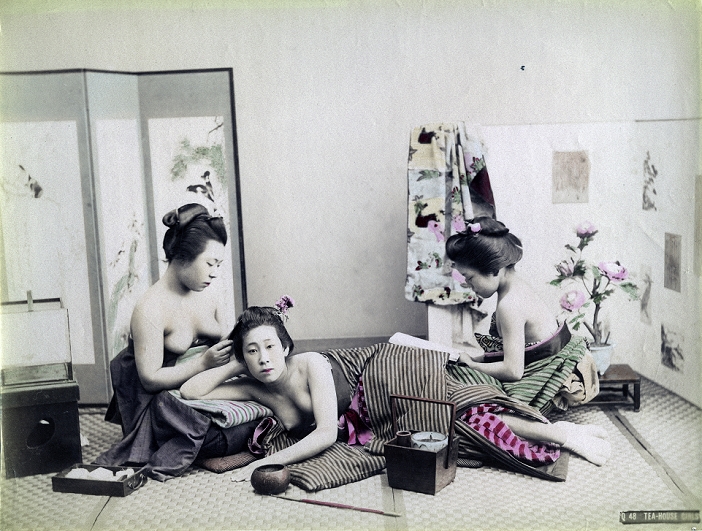 Half naked woman  date unknown  A woman is lying half naked on the floor, her head is resting on the knees of another woman who is combing her hair. A third woman is reading something.There is a tobacco tray and a kiseru pipe in front of her. On the left is an andon lamp. Behind them there are two screens.