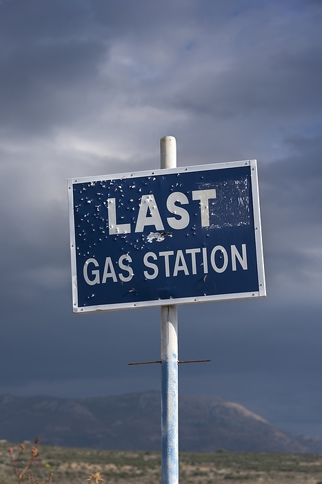 Gas Station Roadsign Clouds gather around a bullet riddled road sign indicating the last petrol station before the end of the Mani peninisular in Greece. The words can also symbolise the idea of the decline of fossil fuels for automobiles, and a switch to more environmentally safe and sustainable forms of transport.
