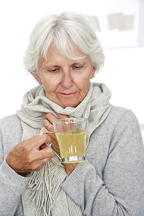 Elderly woman drinking hot lemon A 73 year old woman drinking hot lemon and wearing a scarf to keep warm.