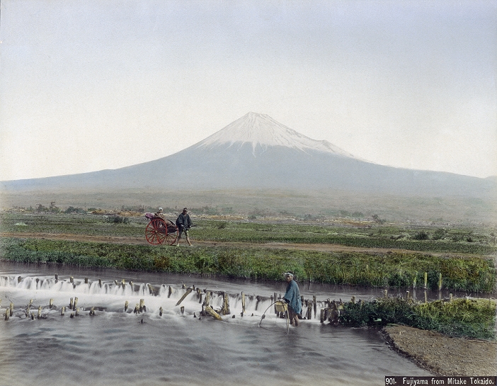 Mt. Fuji  1890s  View of Mt. Fuji on the Tokaido. The caption calls the place Mitake.  As Mount Hoei is clearly visible on the right, this must be nearby Yoshiwara Juku in Shizuoka Prefecture, the fourteenth station on the Tokaido. Going from Edo to Kyoto, this was the only area along the Tokaido where Mount Fuji was seen on the left. The area was known as  Hidari Fuji   Left Fuji .  In the foreground, a man is fishing in a river, while another is pulling a rickshaw with a passenger. Albumen photograph by Kusakabe Kimbei, 1890s.  Negative title: 901. Fujiyama from Mitake Tokaido. 