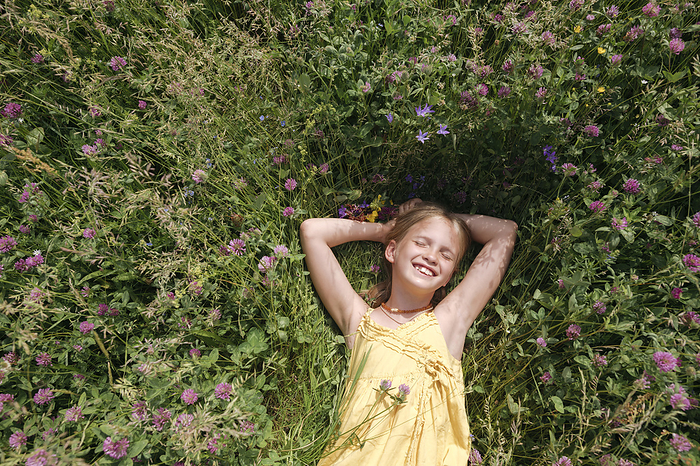 Portrait of happy little girl with eyes closed lying on a meadow in summer