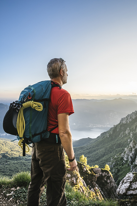 Hiker with backpack looking at mountains against clear sky during sunset, Orobie, Lecco, Italy