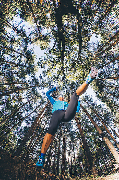 Mature woman jumping against trees in forest